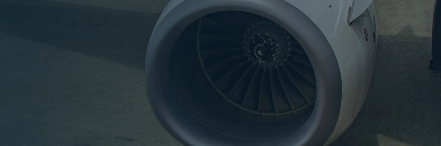 Close-up view of a jet engine on an airplane. The image shows the fan blades starting to spin, with a clear view of the engine's structure. The aircraft is on the ground, and the tarmac is visible.