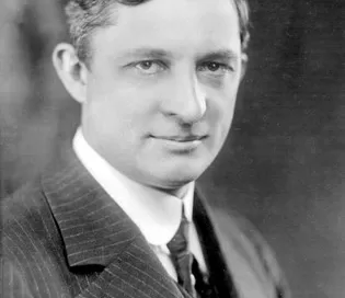 A black and white photo of a man in a suit and tie, looking into the camera with a neutral expression, subtly captures the essence of a Softinway engineer poised at the forefront of turbomachinery innovation.