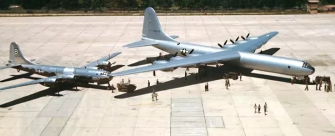 Two large military aircraft parked on an airport runway, with one significantly larger than the other, surrounded by a few people on the ground.
