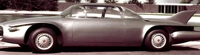 A vintage, futuristic-looking concept car with a sleek silver body, bubble canopy, and large rear fin displayed outdoors.
