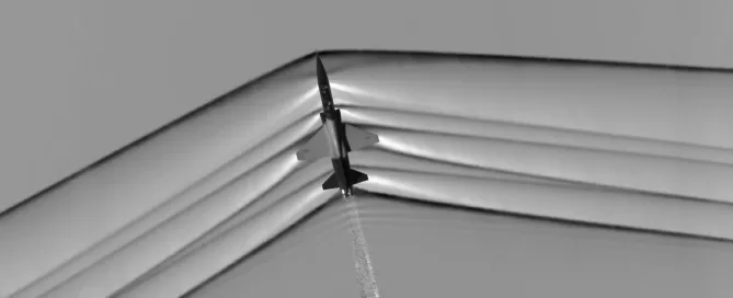 A jet aircraft breaking the sound barrier with visible shockwaves, viewed from below in a grayscale image.