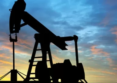 Silhouette of an oil pump jack against a colorful sunset sky.