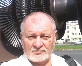 A man with a beard stands outside in front of large industrial turbomachinery under a clear sky, embodying the innovative spirit of Softinway.