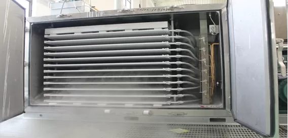 Industrial freeze dryer with open door showing multiple metal shelves and steam inside.