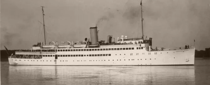 A vintage black and white photo of a large passenger ship on calm water, with two tall masts and a central smokestack emitting smoke.