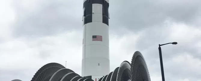 A large rocket is vertically positioned against a cloudy sky; turbine-like machinery is visible in the foreground.