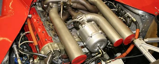 Close-up view of a high-performance car engine with multiple pipes and components, enclosed in a red-painted area.